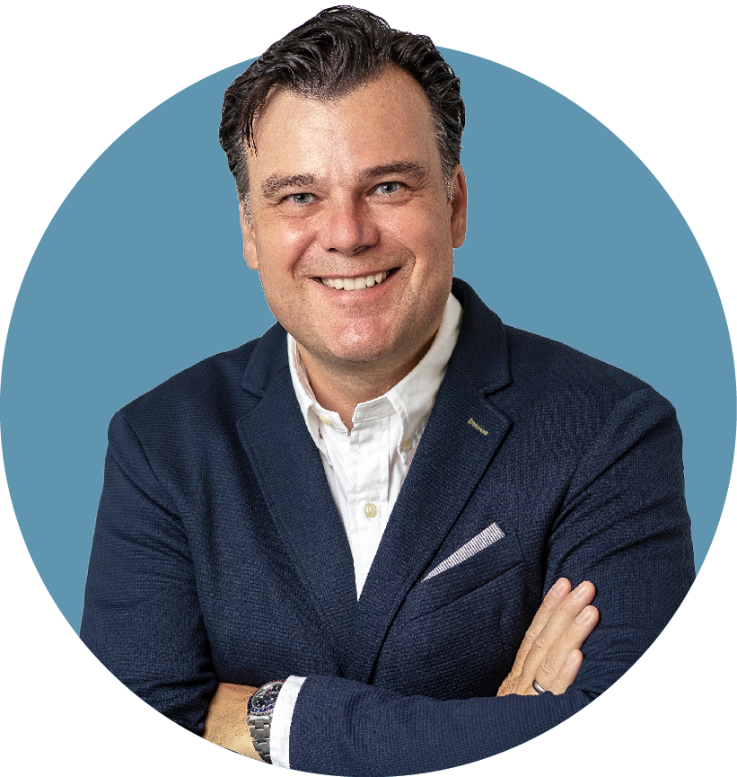 Porträt von Robert Käß, Aufsichtsrat der audius SE, lächelnd in dunklem Sakko und weißem Hemd vor blauem Hintergrund.