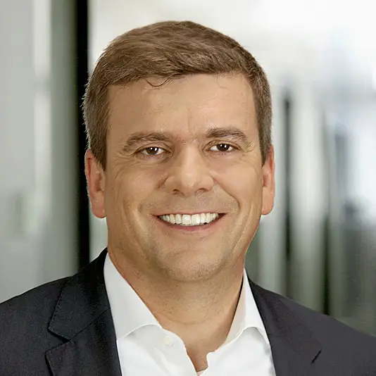 Porträt von Rainer Francisi, Vorstandsmitglied der audius SE, lächelnd in dunklem Sakko und weißem Hemd.