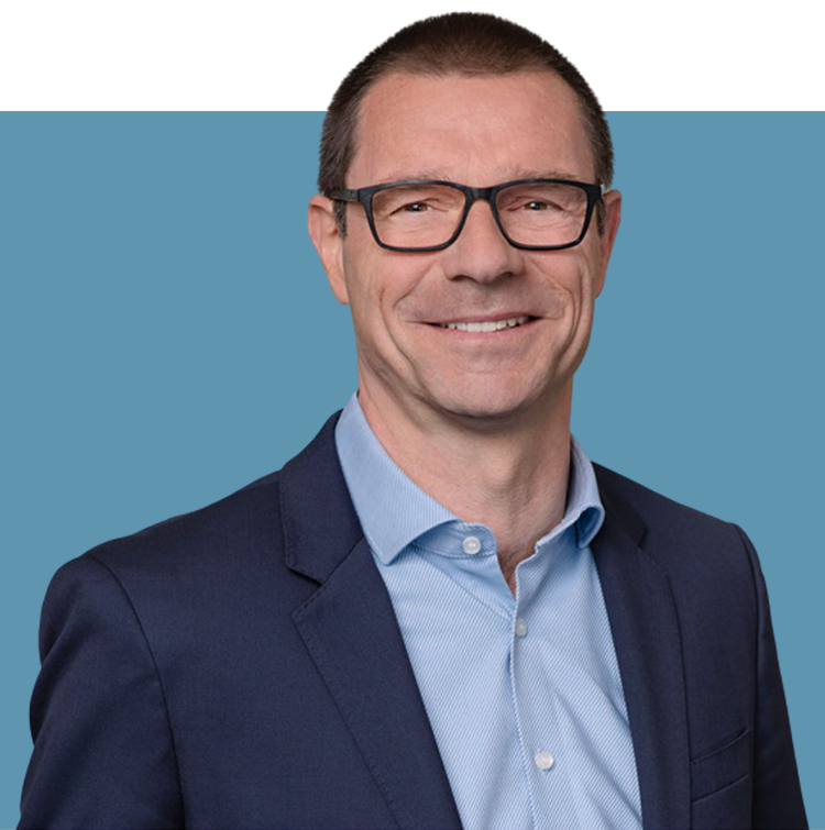 Porträt von Matthias Kraft, Vorstandsmitglied der audius SE, lächelnd in dunklem Sakko und blauem Hemd vor blauem Hintergrund.