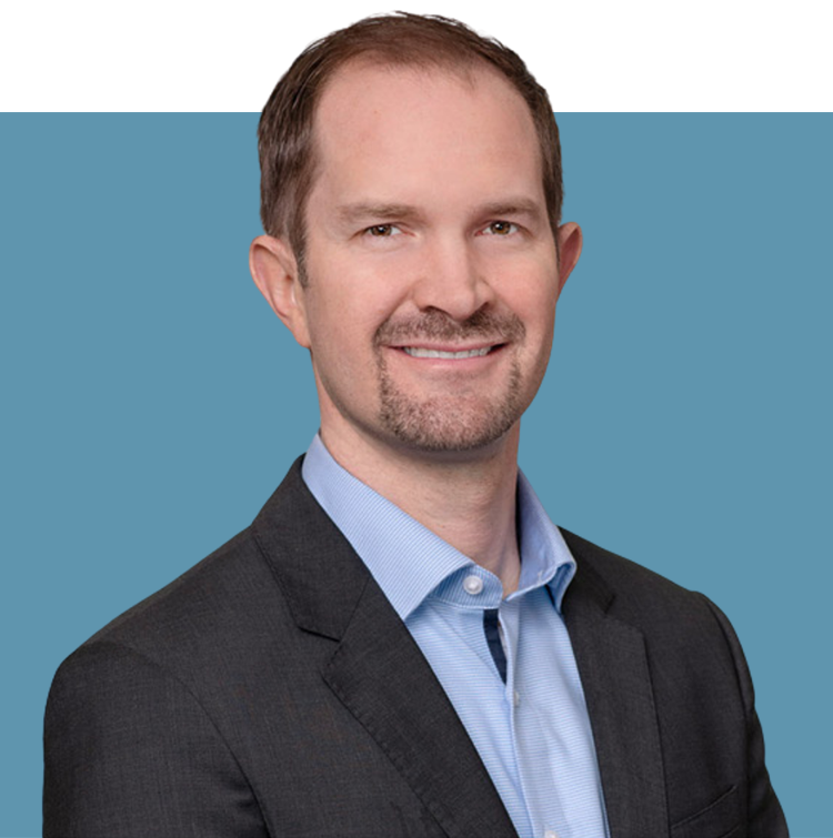 Porträt von Wolfgang Wagner, Vorstandsmitglied der audius SE, lächelnd in dunklem Sakko und blauem Hemd vor blauem Hintergrund.