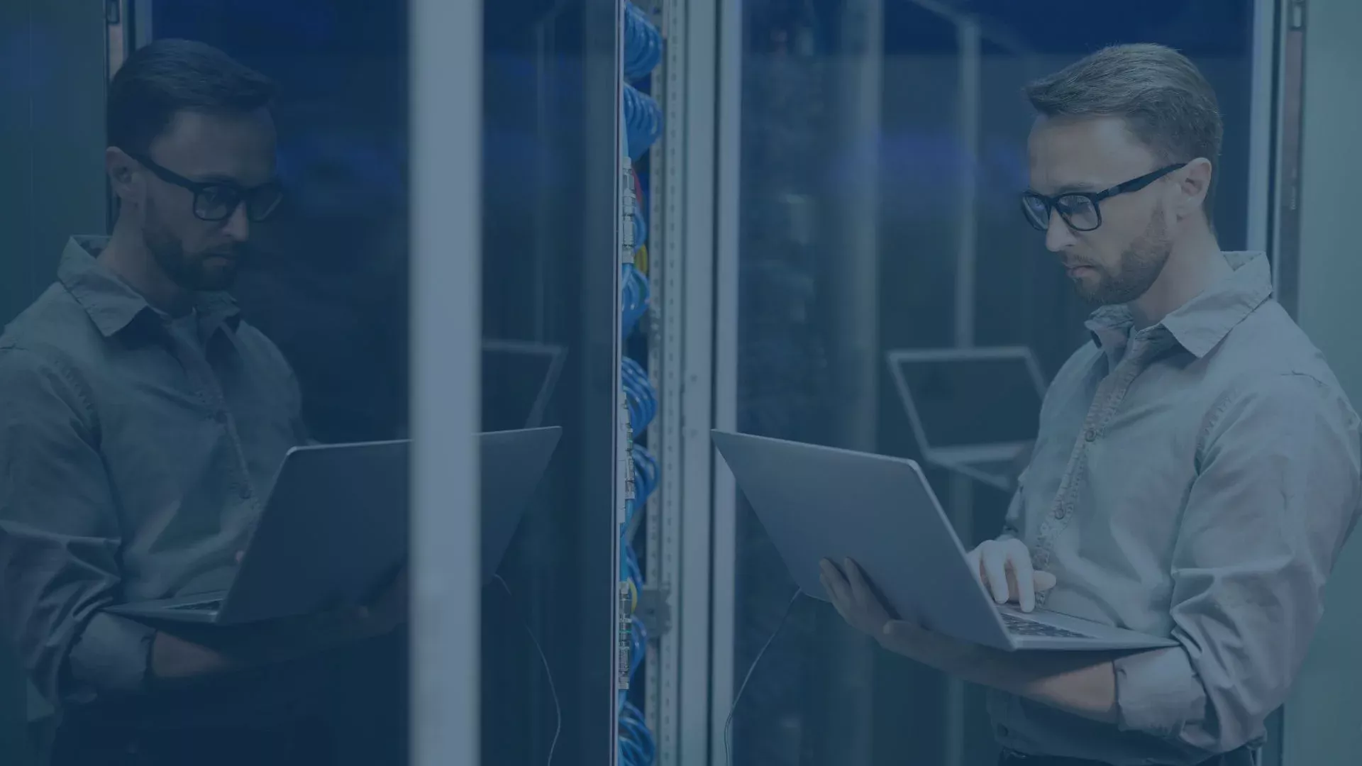 IT-Techniker arbeitet mit einem Laptop im Serverraum vor einem Rack mit Netzwerk- und Serverhardware.