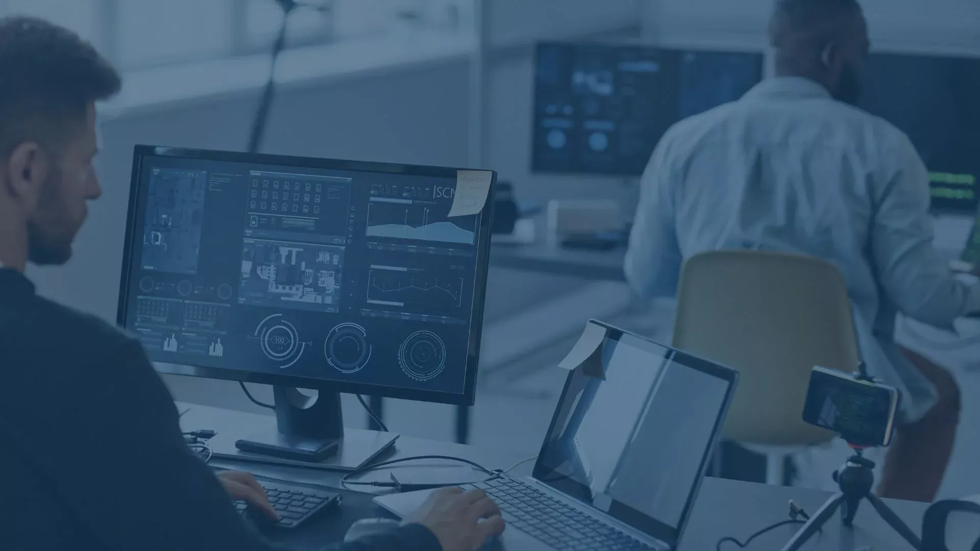 IT-Mitarbeiter arbeiten an Monitoren mit technischen Dashboards und Systemanalysen in einem modernen Büro.