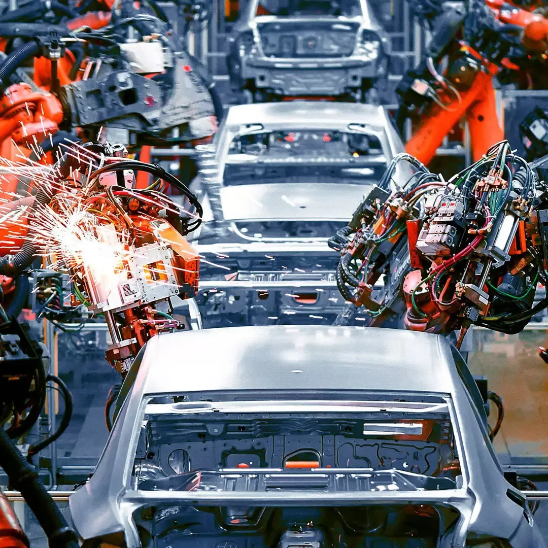 Roboterarme schweißen Karosserieteile in einer Autofabrik (symbolisiert industrielle Automation und digitale Transformation in der Fertigung).