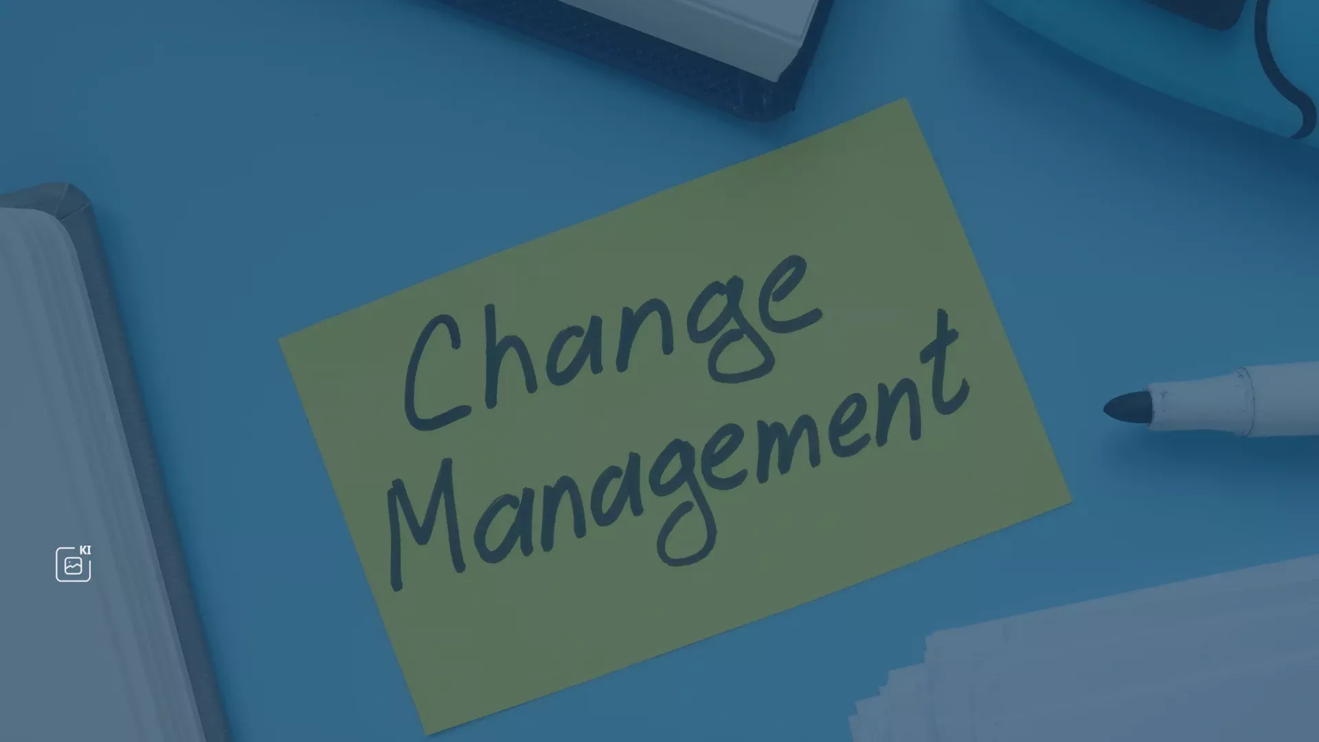 Stift und Notizblock auf blauem Hintergrund mit einem grünen Zettel, auf dem handschriftlich 'Change Management' steht – Symbol für die Bedeutung von Change Management bei der Einführung von Microsoft 365, um Nutzung, Produktivität und Zusammenarbeit zu optimieren und Schatten-IT zu vermeiden.